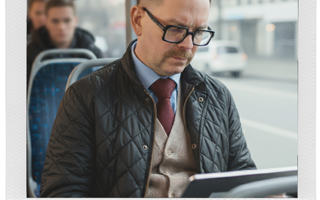 Man med glasögon och kavaj som använder en surfplatta på en buss.