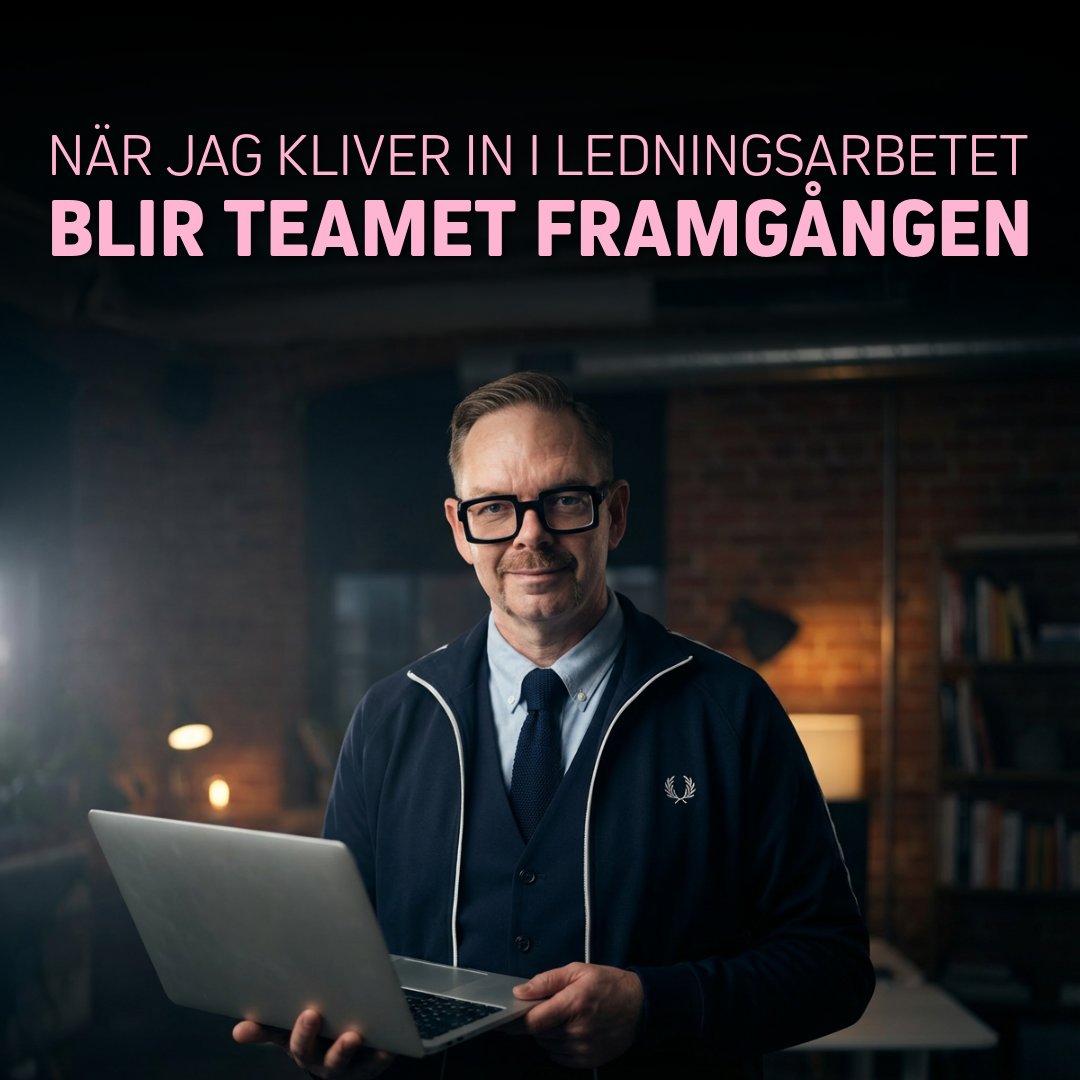 Man med glasögon och laptop i handen, klädd i mörkblå tröja och vit skjorta, står i ett kontorsrum.