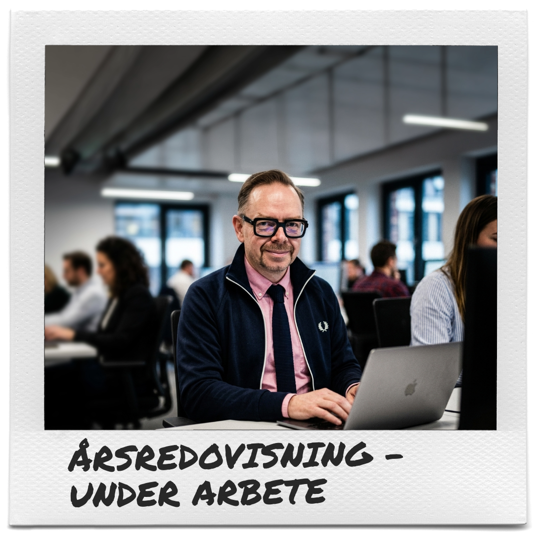 En man med glasögon i mörkblå jacka och rosa skjorta sitter vid en laptop i ett kontorslandskap. Polaroidramen runt bilden visar texten ÅRSREDOVISNING – UNDER ARBETE.