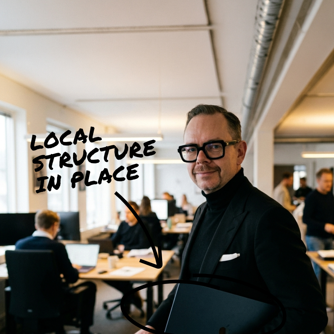c-by-partner kontorsmiljö med man i svart kostym och glasögon; tydlig text Local Structure in Place över bilden framhäver fokus i professionell miljö.